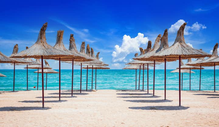 Photo of Mangalia, Romania. Sandy beach of the Black Sea with straw beach umbrellas on a clear, blue sky, sunny summer day.