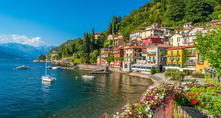 Flowery fence and colorful mediterranean buildings on the waterfront. Anchored boats in the harbor of Varenna, lake Como, Lombardy, Italy, Europe
