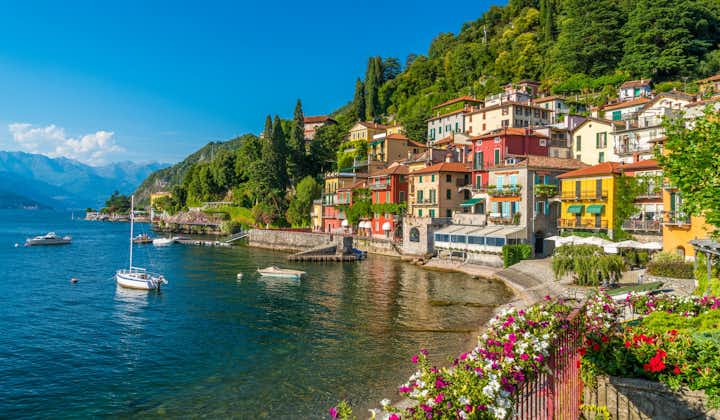 Flowery fence and colorful mediterranean buildings on the waterfront. Anchored boats in the harbor of Varenna, lake Como, Lombardy, Italy, Europe