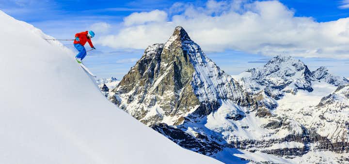 photo of skier skiing downhill in high mountains in fresh powder snow. Snow mountain range with Matterhorn in background. Zermatt Alps region Switzerland.