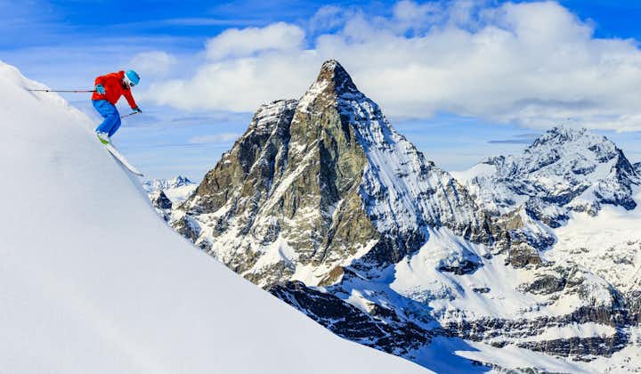 photo of skier skiing downhill in high mountains in fresh powder snow. Snow mountain range with Matterhorn in background. Zermatt Alps region Switzerland.