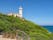 Capo Circeo Lighthouse, white tower on the slope of mountain in the blue sky background, next to the San Felice Circeo town in Italy. Beautiful Italian landscape.
