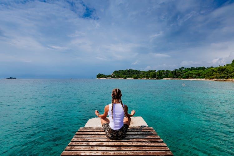 Photo of girl sitting in yoga pose at the Pier at Rovinj, Croatia.