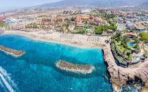 photo of aerial shot of Costa Adeje area, South Tenerife, Spain. Captured at golden hour, warm and vivid sunset colors. Luxury hotels, villas and restaurants behind the beach.