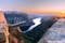 A man sits while throwing his arms in the air on the mountain's cliff edge of Trolltunga throning over Ringedalsvatnet watching the sunset in the snowy Norwegian mountains near Odda, Rogaland, Norway