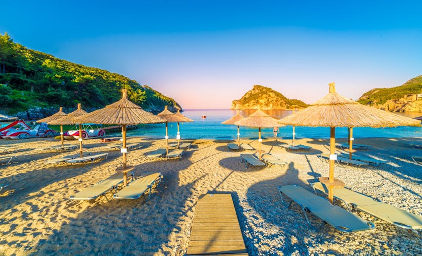 Photo of beach, chairs and umbrellas at sunrise in Paleokastritsa village, Corfu island, Greece.