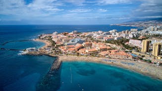 photo of aerial shot of Costa Adeje area, South Tenerife, Spain. Captured at golden hour, warm and vivid sunset colors. Luxury hotels, villas and restaurants behind the beach.