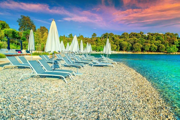 Photo of  gravel beach and seashore. Sun loungers and beach umbrellas at sunset on the beach, Rovinj, Istria region, Croatia.