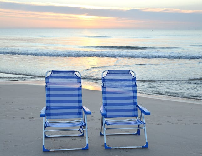 Photo of sunrise with Two empty beach chairs on Sant Joan D'Alacant beach in Alicante province Costa Blanca region of Spain.