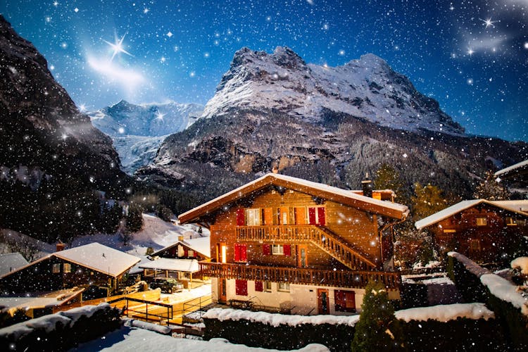 Photo of winter night Grindelwald snowy mountain, stars and wooden house.