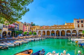 Photo of Old harbour Porto Vecchio with motor boats on turquoise water, green trees and traditional buildings in historical centre of Desenzano del Garda town, Northern Italy.