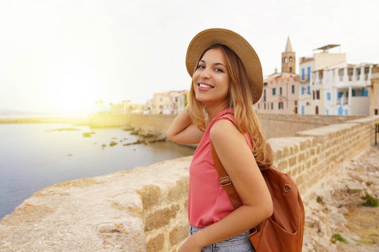 Portrait of smiling relaxed traveler woman walking along Alghero seafront, Sardinia, Italy.