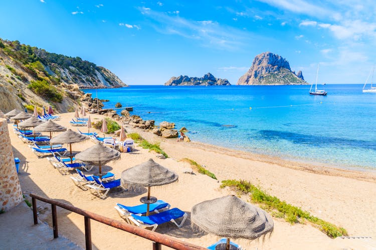 Photo of  Cala d'Hort beach with sunbeds and umbrellas and beautiful azure blue sea water, Ibiza island.
