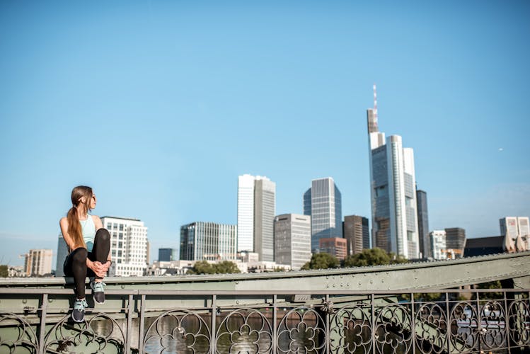 Photo of tourist woman sitting on the bridge with great view on the modern city of Frankfurt.