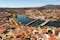 Photo of scenic aerial view of Mirandela city with residential houses with brownish tiled roofs, bridges crossing Tua river and water fountain on spring day, Braganca, Portugal.