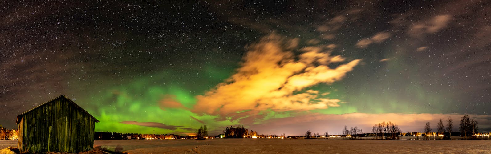 Panorama of green lights Aurora and stars shine over abandoned shed standing alone in the field, Umea city, Sweden.